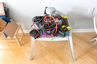 A collection of exercise equipment including a gray dumbbell, resistance bands in various colors, black workout gloves, and green arm/ankle weights on a white plastic step platform.