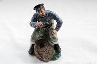 Front angled view of Royal Doulton 'The Lobster Man' figurine showing the fisherman holding a lobster crouched on a lobster trap.
