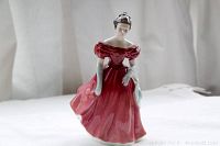 Full view of porcelain figurine showing the woman in a flowing red dress, standing on a flat surface with curtain background.