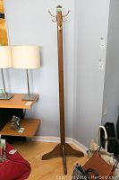 Full view of the wooden coat stand placed in a room corner next to shelves and bags on floor.