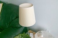 First image showing one lamp standing on a table beside a green couch, beige pleated shade, tripod-style dark metal base, untested condition.