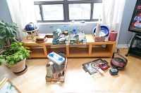 Wooden shelf unit with three open compartments positioned horizontally, various items placed on and around it, including plants and decorative objects, items not included in sale.