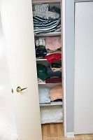 Photo of closet shelf packed with various folded linens including blankets and towels in assorted colors and fabrics.