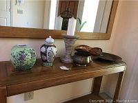 Wooden console table with porcelain vases, metal decorative items, and marble pedestal.