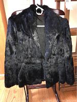 Photo of black rabbit fur coat displayed on wooden chair, showing texture and sheen of fur jacket.