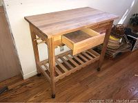 Full view of the wooden kitchen island showing butcher block top, one drawer open, lower slatted shelf, and casters on legs.
