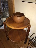 Two round solid wood tables stacked; a decorative wooden bowl placed on top of the upper table.