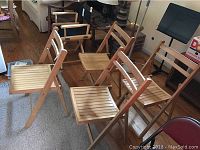 Four wooden folding chairs placed in a living room setting, showing their overall design and wood grain finish.