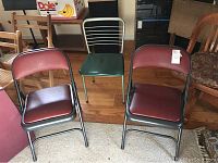 Three metal chairs are shown: two maroon folding chairs with vinyl seats and one green metal chair with slatted backrest.