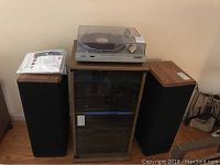 Two tall Audio Research floor speakers on either side of a wooden cabinet with multiple audio components inside, topped with a vinyl record player with a clear dust cover.