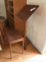 Wooden music stand paired with bench shown standing on hardwood floor next to bookshelf and chair, highlighting the wood finish and design.