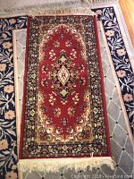 Rug with red central floral medallion and intricate borders, cream fringes at ends.