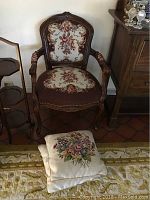 Front view of one embroidered needlepoint chair with floral designs and two matching pillows on floor in front of it.