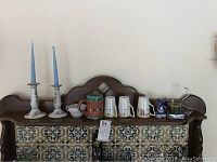Shelf with two candlesticks with blue candles, multiple ceramic mugs, and creamers