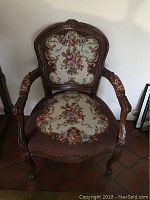 Front view of antique wooden armchair with needlepoint upholstery showing floral design on seat and backrest.