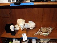 Two classical-style white sculptures and a decorative porcelain wall clock on a wooden surface.