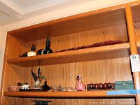 Three shelves with various carved, ceramic, and wooden decorative items including duck decoys, pig figurine, bead decoration, and a blue metal box.