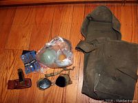 Photo of U.S. Army canvas bag, two knives in leather sheaths, military goggles, bagged items including straps and small accessories.