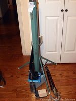 Green metal adjustable tripod stand with a large 45 inch screen mounted. Includes a black carrying strap, a blue box labeled 'ScreenVac', and metal mounting accessories.