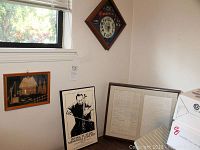 Photo showing a corner of the room with the ship artwork, framed historical document on the floor, black and white concert poster, and diamond-shaped clock on the wall.
