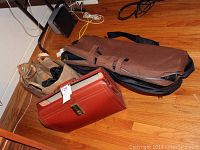 Three soft cases placed on wooden floor, including brown canvas, black nylon, and tan fabric cases, showing overall condition and size
