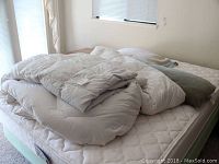 Photo showing a white duvet and gray duvet stacked on a mattress, daylight from window illuminating the scene, visible tag on the white duvet shows The Company Store brand.