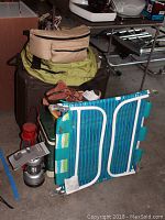 Photo of stacked camping gear items including suitcases, cooler, chair, boots, and lanterns in garage