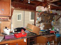 View of garage counter with various toolboxes, plastic organizer trays, and scattered hand tools alongside a cardboard box and bags