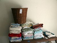 Wicker hamper placed on top of stacks of folded sheets, showing full collection.