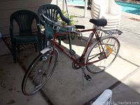 Red Schwinn LeTour Tourist bicycle with 24 inch wheels, shown parked on driveway near plastic chairs and pool area.