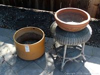 Wide view showing large orange decorative garden pot on top of gray wicker table; medium yellow pot beside them.
